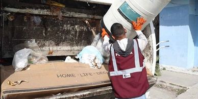 Worker wearing gloves throws trash into a garbage truck.