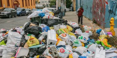 Overflowing garbage bags and trash litter a city street, creating an unsanitary scene.