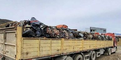 A truck loaded with a large pile of crushed and compacted scrap metal.