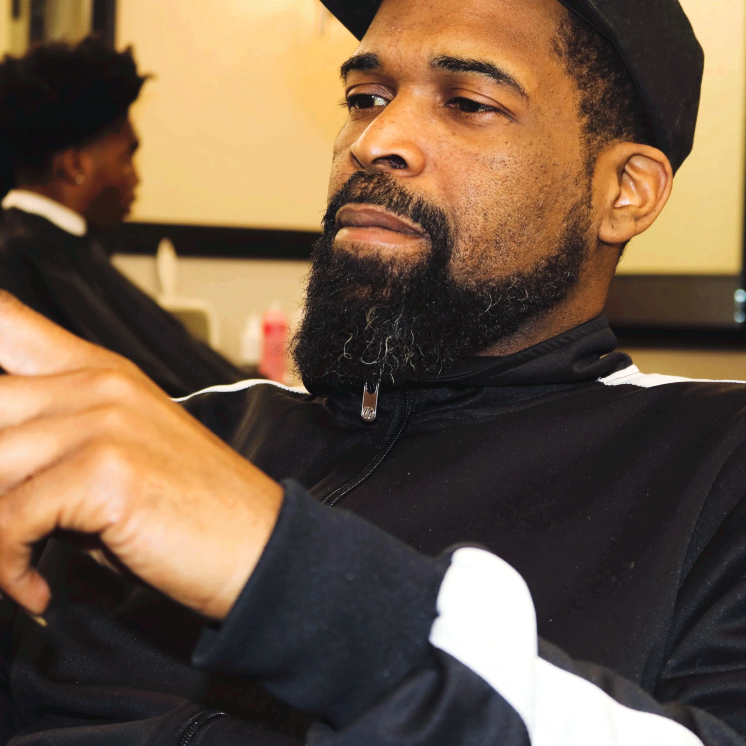 Man with a beard in a black jacket and cap looking thoughtfully.