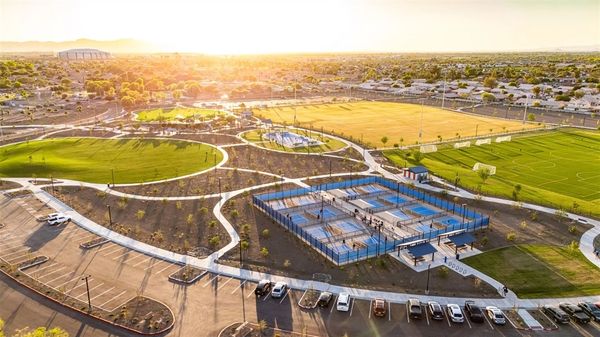 Aerial view of a sports complex at sunset with tennis courts and open fields.