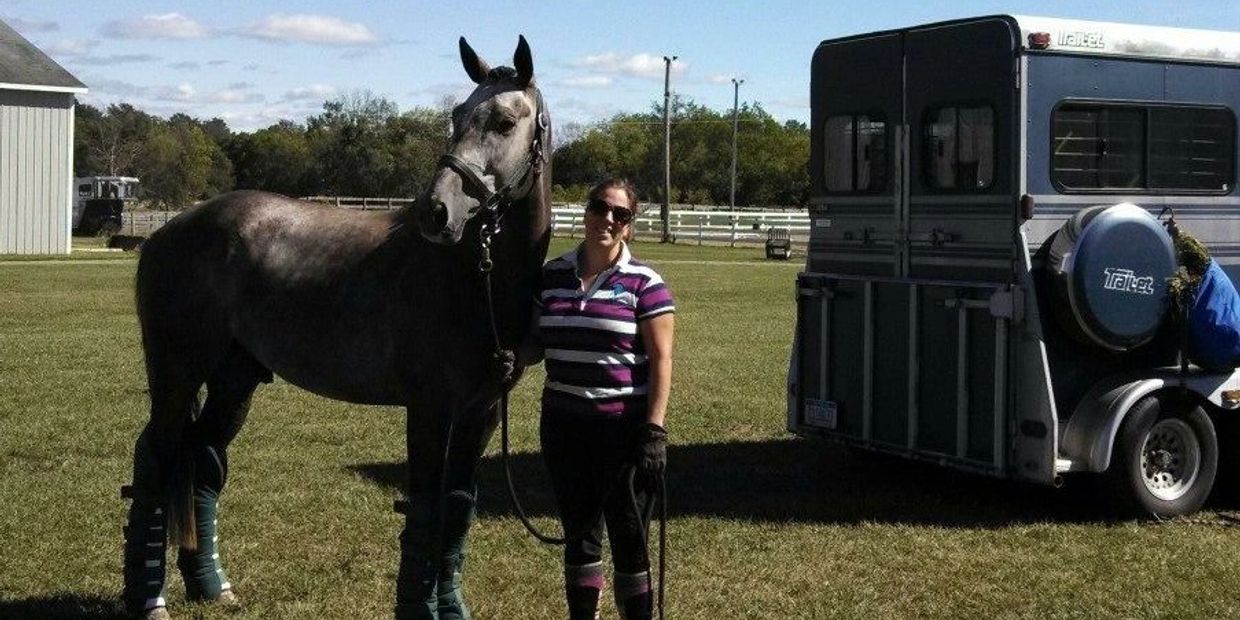 Woman standing with a horse next to a horse trailer.