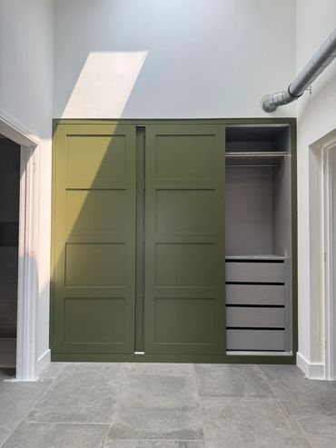 Modern closet with olive green sliding doors and built-in drawers inside.