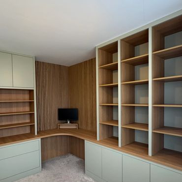 Modern corner office setup with wooden shelves and soft green cabinetry.