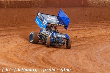 Blue sprint car racing on dirt track.