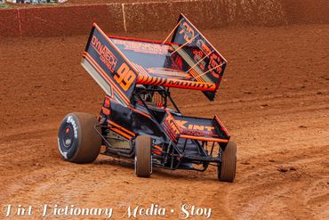Orange sprint car racing on dirt track.