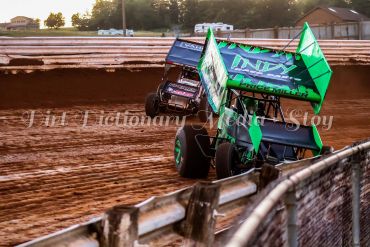Two sprint cars racing on a dirt track during sunset.