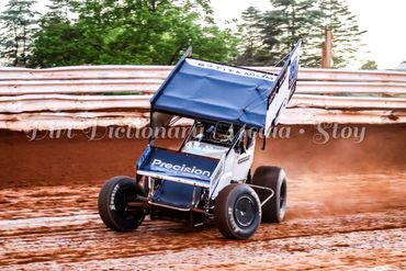 A sprint car racing on a dirt track with a blue wing.