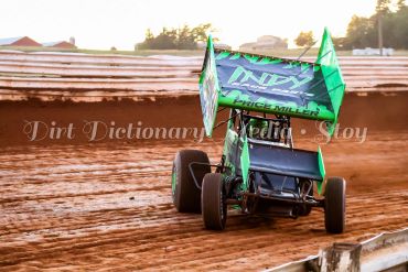 Green sprint car racing on a dirt track during sunset.