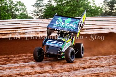 Sprint car racing on a dirt track during a race.