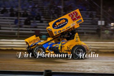 Orange sprint car racing on a dirt track at night.
