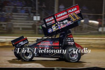 Black sprint car racing on dirt track at night.