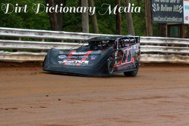 Black dirt late model race car speeding on a dirt track.