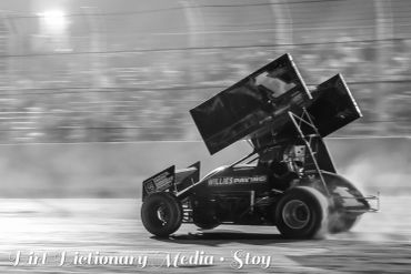 Black and white photo of a sprint car racing on a dirt track at speed.
