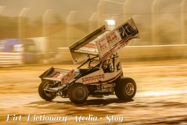 A sprint car racing on a dirt track at night.