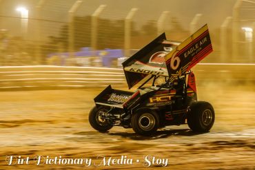 A sprint car racing on a dirt track at night.