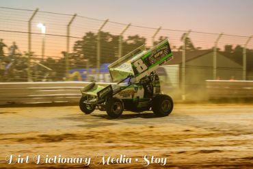 Sprint car racing on a dirt track during sunset.