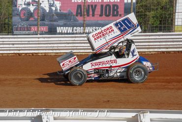 A sprint car races on a dirt track during a motorsport event.