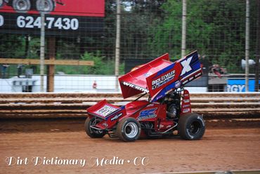 Red sprint car racing on a dirt track at speed.