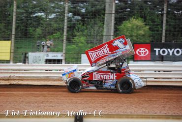 Red and white sprint car racing on a dirt track.