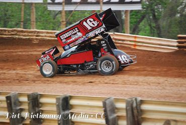 A red and black sprint car racing on a dirt track.