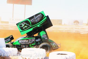 Green and black sprint car racing on a dirt track kicking up dust.