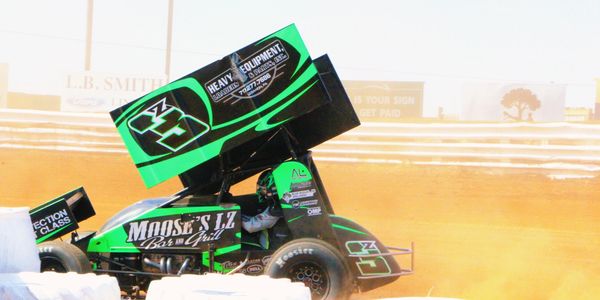 Green and black sprint car racing on a dirt track.