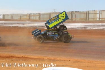 Sprint car number 39 racing on a dirt track, kicking up dust.