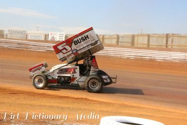 A sprint car racing on a dirt track under a clear sky.