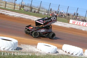 Black sprint car racing on a dirt track with visible spectators.