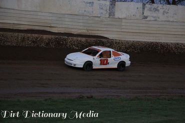 White race car number 10 racing on a dirt track at dusk.