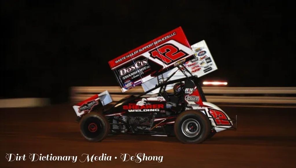 A sprint car racing on a dirt track at night.