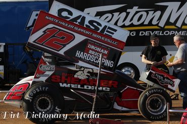 A black and red sprint car with number 12 in a garage area.