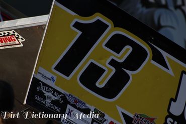 Close-up of a race car wing with number 13 and sponsor stickers.