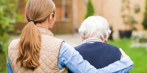 Young woman supporting elderly woman outdoors.