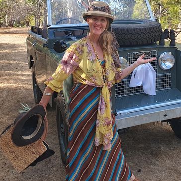 Woman in vibrant clothes poses by vintage off-road vehicle.