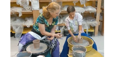Woman teaching child pottery using a wheel in a workshop.