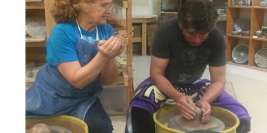 Two people shaping clay on pottery wheels in a workshop.