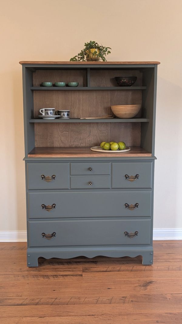 Blue wooden cabinet with shelves, bowls, cups, and green apples on a plate.