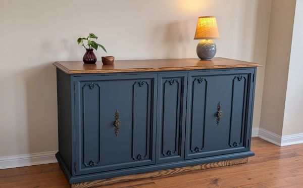 Blue vintage cabinet with wooden top, decorated with a lamp and small plants.