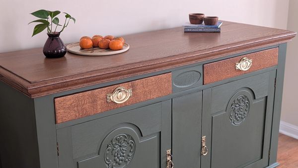 Elegant wooden sideboard with decorative carvings and brass handles, topped with a plant, plate of oranges, and cups.