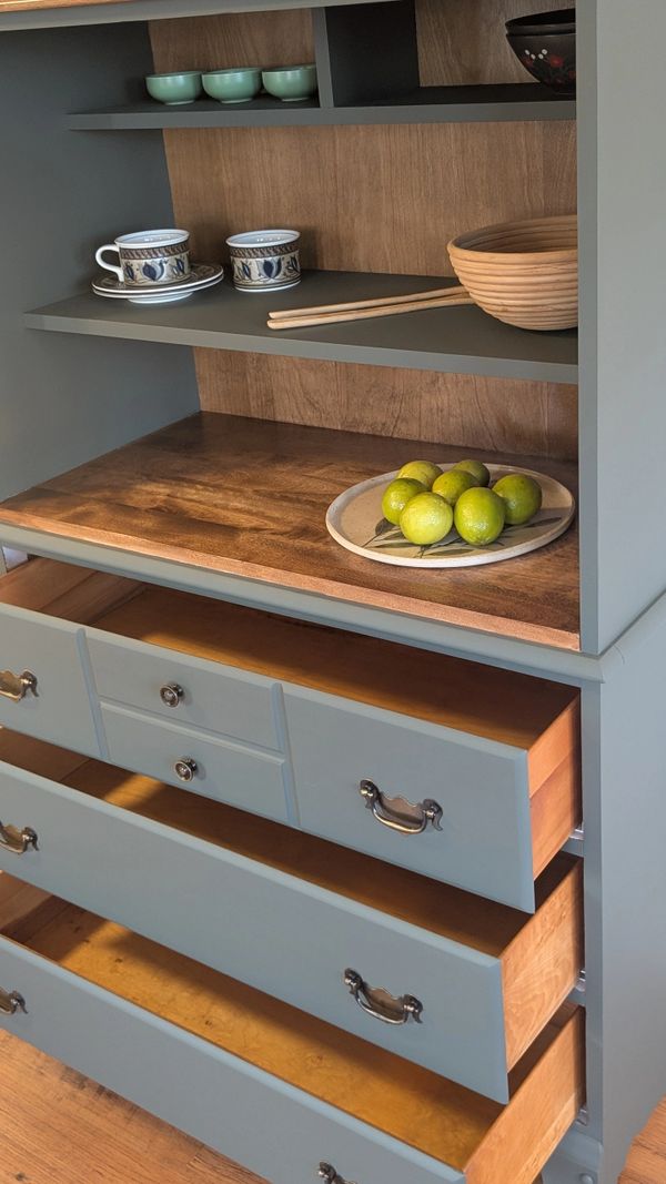 A gray cabinet with open drawers, cups, bowls, and a plate of limes.