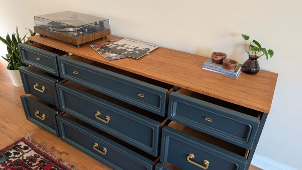 A wooden dresser with partially open blue drawers and decor on top.