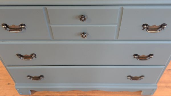 Close-up of a gray wooden dresser with metal handles on a wooden floor.