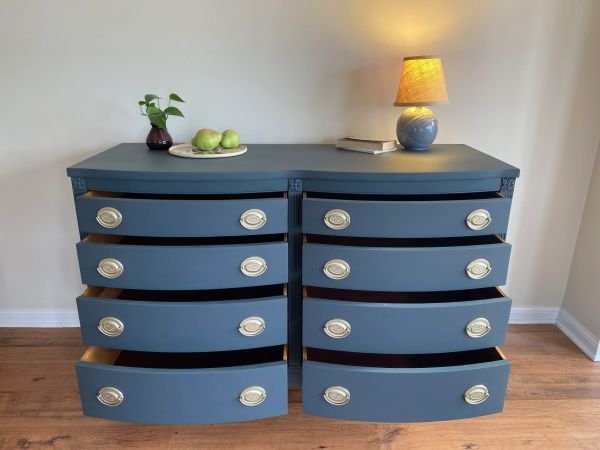 Blue dresser with open drawers, decorated with a lamp, plant, and fruit plate.