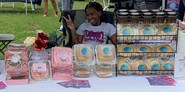 A young girl happily selling treats at a booth in an outdoor market.