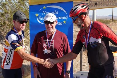 photo of two male cyclists shaking hands while another wearing a medal looks on