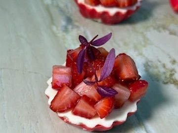 Mini strawberry tarts with purple garnish.