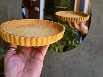 Hand holding an empty tart crust with a reflection in a round mirror.