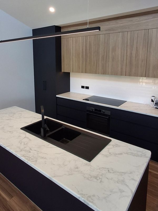Modern kitchen with black cabinetry, marble countertops, and wood accents.